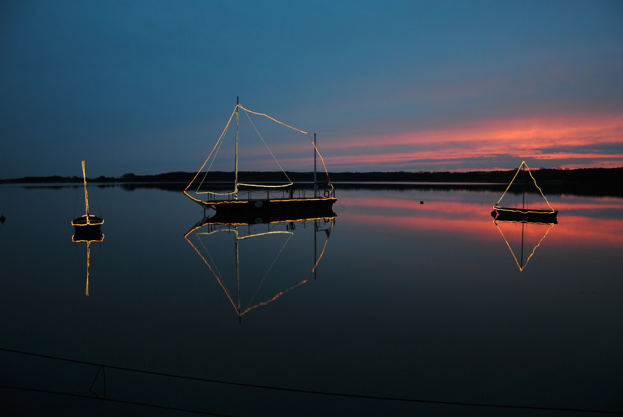 drei Bootssilhouetten vor einem rot blauem Sonnenuntergang
