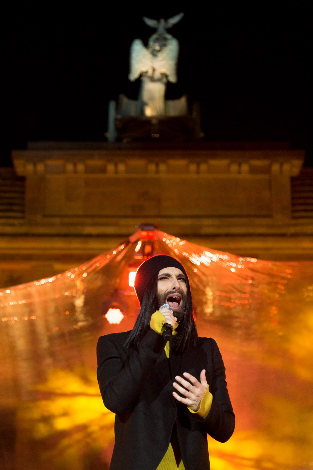 Conchita Wurst singt in gelbem Licht vor dem Brandenburger Tor