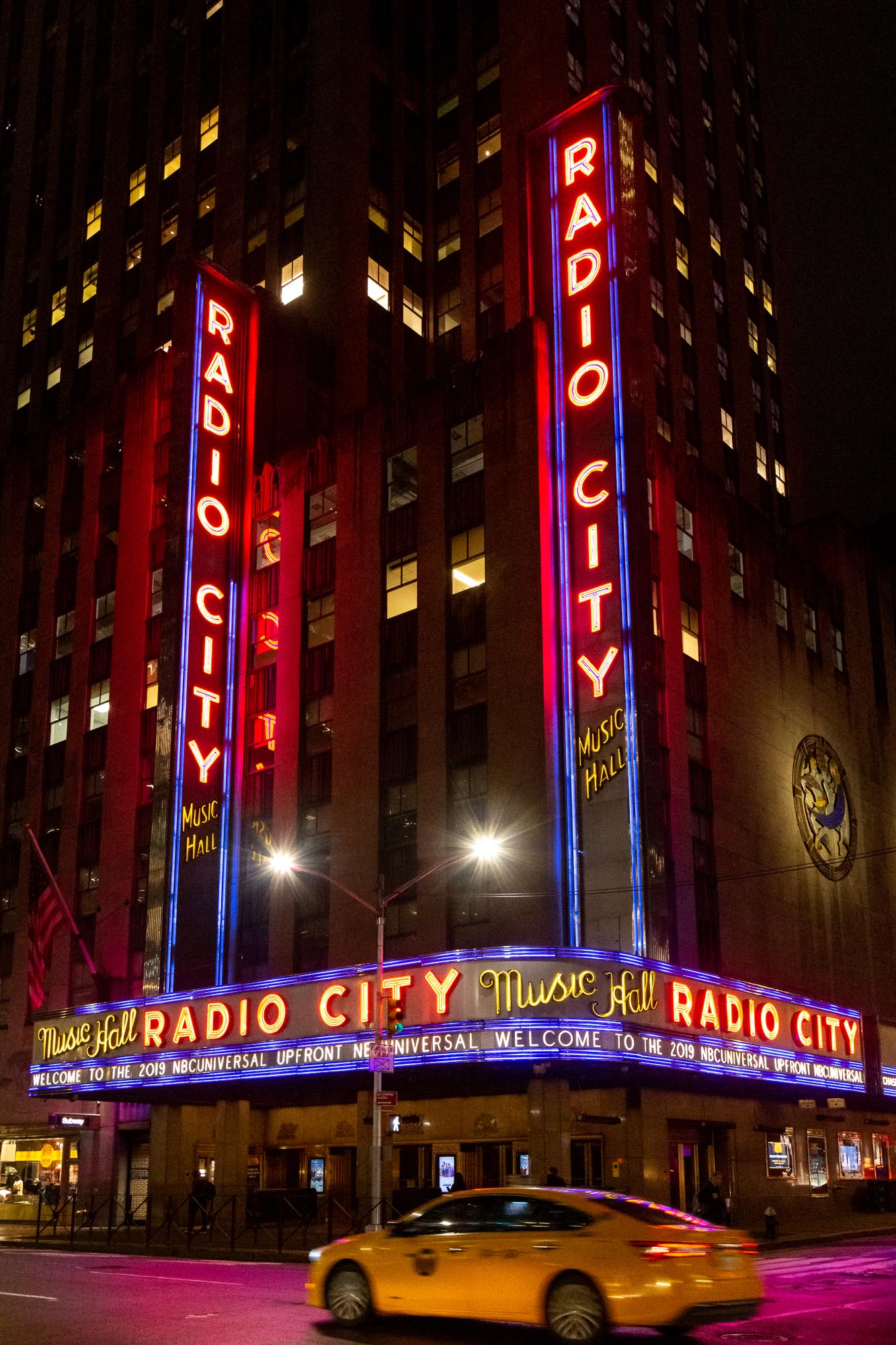 Radio City Music Hall bei Nacht mit gelbem Taxi im Vordergrund